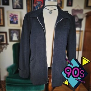 May include: A dark gray jacket with a silver zipper, a collar, and a small pocket. The jacket is displayed on a mannequin with a black choker necklace. The image has a 90s theme graphic in the bottom right corner.