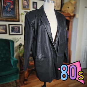 May include: A black leather blazer with a single-button closure, displayed on a mannequin. The blazer has a classic lapel and two front pockets. The image includes a colorful "80s" graphic in the bottom right corner.