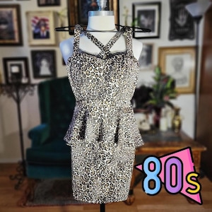 May include: A leopard print dress with a peplum waist and crisscross straps. The dress is displayed on a mannequin. The image has a vintage aesthetic, with a colorful "80s" graphic in the corner.