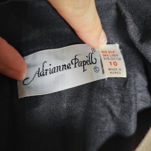 May include: Close-up of a label from Adrianne Papell clothing. The label is white with black text, including the brand name and size 10. Fabric composition details are also visible: 35% silk, 34% linen, and 31% cotton. The label reads "Made in Korea."