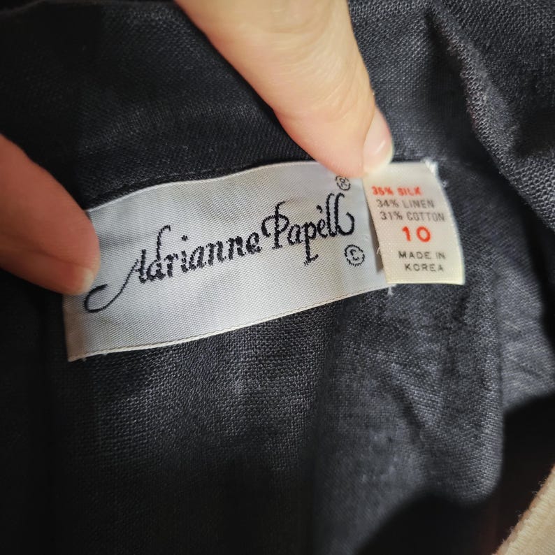 May include: Close-up of a label from Adrianne Papell clothing. The label is white with black text, including the brand name and size 10. Fabric composition details are also visible: 35% silk, 34% linen, and 31% cotton. The label reads "Made in Korea."