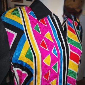 May include: A colorful patterned shirt with a black collar and sleeves. The shirt features a vibrant design with pink, yellow, blue, green, and red geometric shapes and stripes. The fabric has a textured appearance.