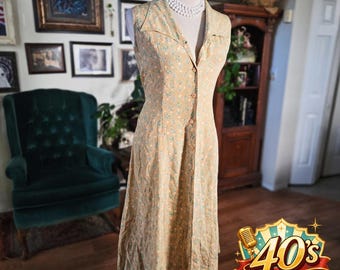 May include: A vintage-style, sleeveless dress in a light tan color with a floral pattern. The dress features a collared neckline, a button-down front, and a midi length. The dress is displayed on a mannequin.