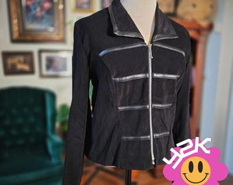 May include: A black jacket featuring a full-length silver zip closure, a pointed collar, and horizontal faux leather trim accents across the chest and torso. The garment is displayed on a mannequin and has long sleeves with a structured fit.