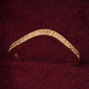 May include: A gold-toned ring with a delicate, intricate design sits in a burgundy velvet ring box.
