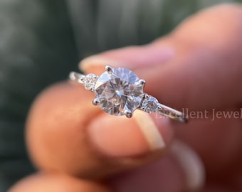 May include: A silver ring with a large round center stone and two smaller stones on either side. The ring is set on a white band.