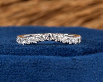 May include: A curved, silver-toned ring set with multiple small, clear gemstones. The ring is displayed on a blue velvet surface, with a blurred brown background.