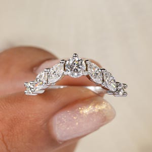 May include: A silver ring with a central round diamond and surrounding marquise-cut diamonds. The ring features multiple clear, sparkling gemstones, creating a delicate and elegant design. The ring is a piece of jewellery.