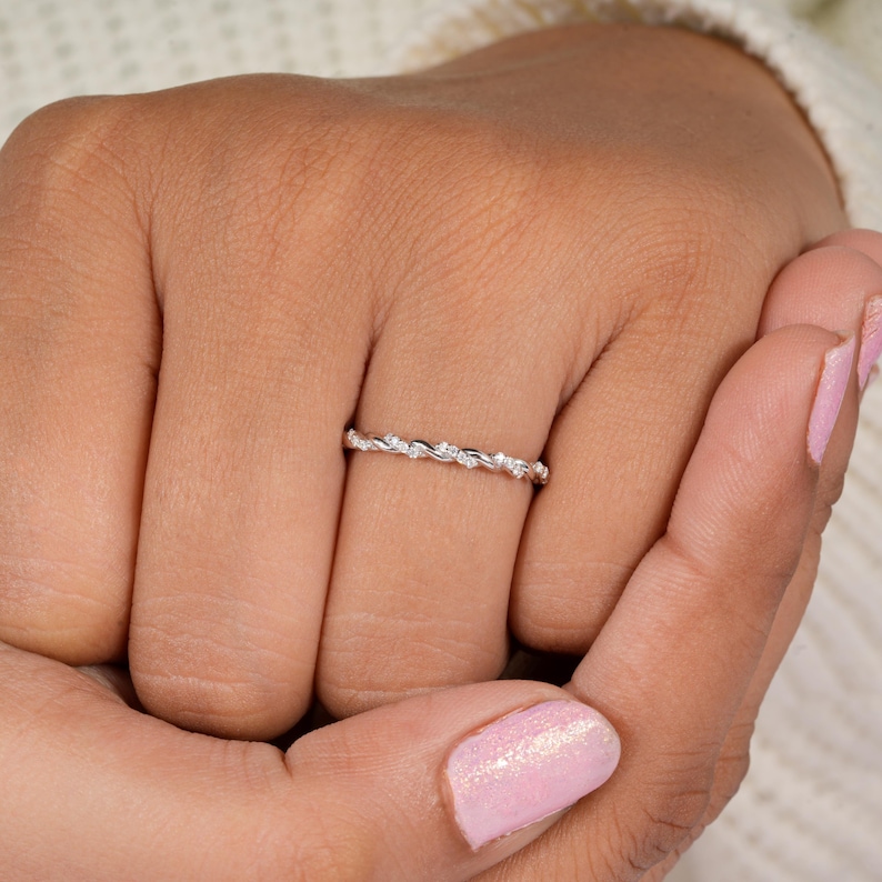 Pu&ograve; includere: Un delicato anello d'argento con un motivo ripetuto di piccole pietre preziose trasparenti. L'anello &egrave; sottile e si trova su un dito, mostrando il suo design intricato. Le pietre preziose sono uniformemente distanziate, creando un effetto scintillante.