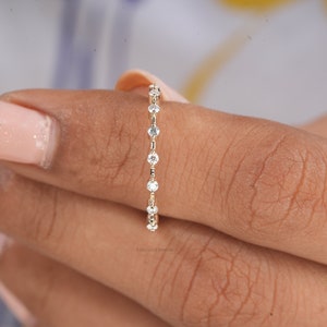 Puede incluir: Un delicado anillo de banda de oro con una fila de pequeñas piedras redondas transparentes.