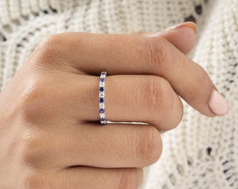 May include: A delicate eternity band ring with alternating blue sapphires and white diamonds set in a silver band.