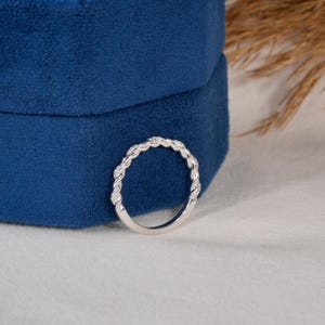 Pu&ograve; includere: Un anello d'argento con un design intrecciato, incastonato con piccole gemme trasparenti. L'anello &egrave; presentato su uno sfondo di velluto blu scuro, forse in un portagioie. I dettagli dell'anello evidenziano la sua lavorazione artigianale.