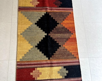 May include: A colorful geometric rug with a black, red, orange, yellow, and brown pattern. The rug has a fringe border.
