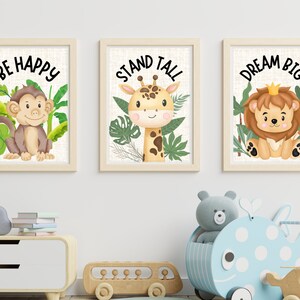 Może przedstawiać: Trzy oprawione wydruki z inspirującymi przesłaniami i ilustracjami kresk&oacute;wek zwierząt. Pierwszy wydruk przedstawia małpę i słowa "Be Happy". Drugi wydruk przedstawia żyrafę i słowa "Stand Tall". Trzeci wydruk przedstawia lwa i słowa "Dream Big".