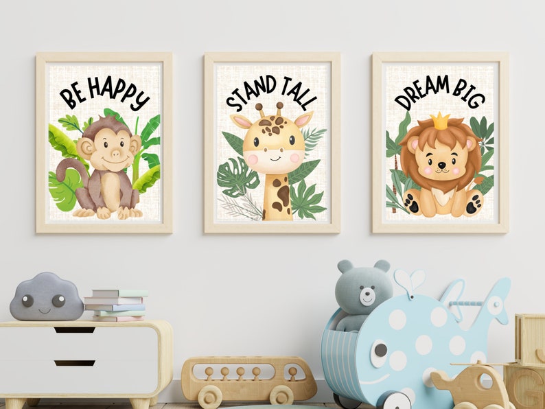 Może przedstawiać: Trzy oprawione wydruki z inspirującymi przesłaniami i ilustracjami kresk&oacute;wek zwierząt. Pierwszy wydruk przedstawia małpę i słowa "Be Happy". Drugi wydruk przedstawia żyrafę i słowa "Stand Tall". Trzeci wydruk przedstawia lwa i słowa "Dream Big".
