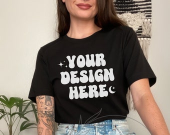 May include: A black t-shirt with the text "YOUR DESIGN HERE" in white, retro-style lettering. The shirt is being worn by a person with a tattoo on their arm.