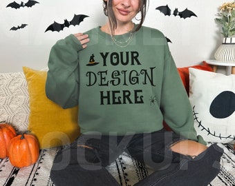 May include: A green sweatshirt with the text "YOUR DESIGN HERE" in black lettering. A small black spider and a witch's hat are also printed on the sweatshirt.