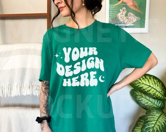 Puede incluir: Una camiseta verde de gran tamaño con el texto "YOUR DESIGN HERE" en una fuente retro blanca.