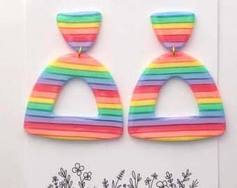 Könnte beinhalten: Regenbogenfarbene Polymer Clay Ohrringe mit einem goldenen Haken. Die Ohrringe sind in Form eines Bogens mit einem kleineren regenbogenfarbenen Oberteil geformt. Die Ohrringe werden auf einer weißen Karte mit dem Text "Elle Bee Clay" präsentiert.