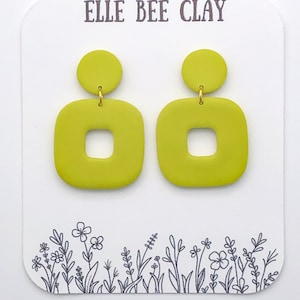 May include: A pair of lime green clay earrings with a square shape and a smaller circle on top. The earrings are on a white card with the text "ELLE BEE CLAY".