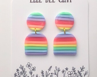 Könnte beinhalten: Regenbogenfarbene, gestreifte Ohrringe aus Polymer Clay mit einem goldenen Haken. Die Ohrringe werden auf einer weißen Karte mit dem aufgedruckten Text "Elle Bee Clay" präsentiert.