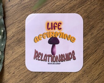 以下が含まれることがあります： オレンジと茶色の文字で「LIFE AFFIRMING RELATIONSHIPS」と書かれた正方形のステッカー。紫色のキノコのイラストが描かれています。ステッカーは薄いピンク色の背景で、ショップの名前が一番下にあります。