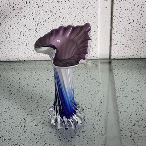 Peut inclure: Un vase en verre violet et bleu avec un design ondulé unique. Le vase a un sommet large et ouvert et une base étroite.