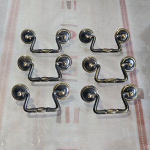 Peut inclure: Huit poignées de tiroir en laiton antique au design simple et élégant. Chaque poignée a un centre arrondi légèrement surélevé et une poignée ouverte incurvée.