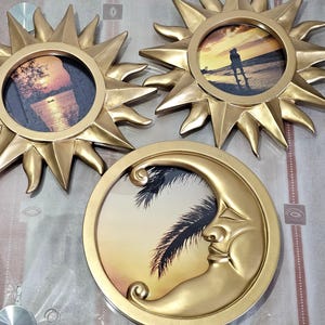 Peut inclure: Trois cadres photo décoratifs : deux en forme de soleil et un en forme de lune. Les cadres solaires sont dorés avec des rayons pointus, chacun contenant une photo circulaire. Le cadre lunaire est doré avec un visage souriant, contenant également une photo circulaire.