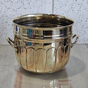 Puede incluir: Un cubo de hielo de metal dorado brillante con dos asas. El cubo tiene un diseño acanalado y es perfecto para enfriar bebidas.