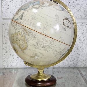 May include: A classic globe with a cream-coloured sphere, showing detailed geographical features. It has a brass meridian and stand, mounted on a dark wooden base. This globe is a decorative item, ideal for home or office display.