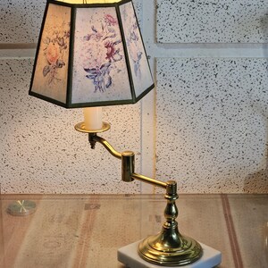 May include: A brass desk lamp with a floral patterned lampshade. The lamp has a flexible arm and a marble base.