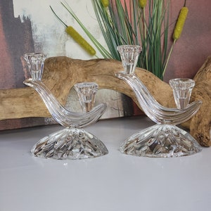 May include: A pair of clear glass candle holders with a curved design and a textured base. The candle holders are on a white surface.