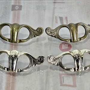 May include: Four ornate brass drawer pulls with a decorative design. The pulls have a curved shape with a central opening.