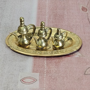 Peut inclure: Trois théières miniatures dorées sur un plateau doré avec un motif orné. Les théières sont de tailles différentes et ont un design traditionnel.