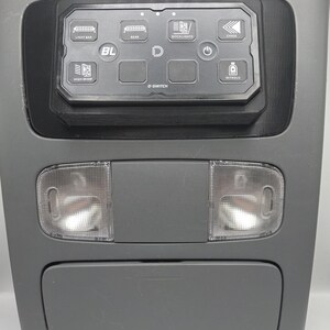 May include: Gray automotive overhead console with integrated lighting and a control panel labeled "D-SWITCH." The panel features illuminated icons for light functions, including "LIGHT BAR," "REAR," and "DITCH LIGHTS."