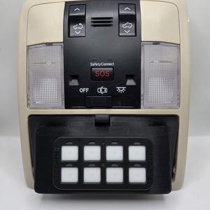 May include: A beige car interior overhead console with black accents. It features buttons for lights, SOS, and other functions. A black panel with eight illuminated square buttons is attached below, with the text "ACR-TOUCH-B".
