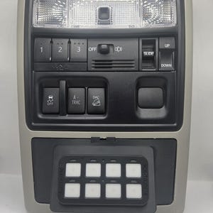 May include: A beige and black automotive overhead console featuring interior lights, a sunroof control switch, and buttons labelled 1, 2, 3, OFF, SLIDE, UP, DOWN, OFF, A-TRAC, and DAC. A black Switch-Pros RCR-TOUCH-8 keypad is mounted on the lower section.