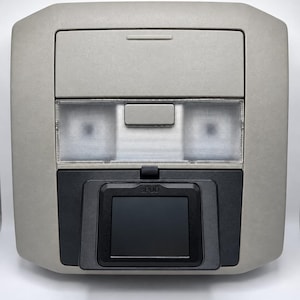 May include: A light gray overhead console for a vehicle featuring a rectangular storage compartment, two clear plastic light lenses with a central switch, and a black sPOD display screen mounted on the lower section with the text sPOD visible.