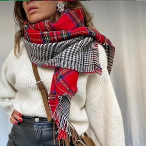 Puede incluir: Una bufanda a cuadros roja, negra y blanca con flecos está drapeada sobre un suéter blanco. La bufanda se combina con pantalones de cuero negros y un bolso bandolera de ante marrón. El atuendo se completa con una correa de cuero marrón.