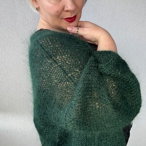 Puede incluir: Un c&aacute;rdigan de punto verde oscuro y peludo con un corte holgado y mangas largas. El c&aacute;rdigan est&aacute; hecho de un hilo suave y ligero y tiene un estilo relajado y casual.