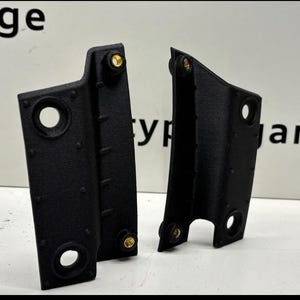 Könnte beinhalten: Zwei schwarze Kunststoff-Autoteile mit goldenen Akzenten. Die Teile haben eine strukturierte Oberfläche und sind wahrscheinlich für den Innenraum eines Autos bestimmt.