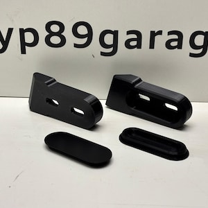 Op de afbeelding: Vier zwarte kunststof onderdelen, twee zijn lang en rechthoekig met twee gaten, en twee zijn ovaal.