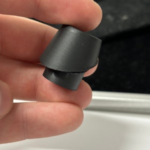 Könnte beinhalten: Ein schwarzer Gummi-Ohrstöpsel in Kegelform. Der Ohrstöpsel ist so konzipiert, dass er Geräusche blockiert.