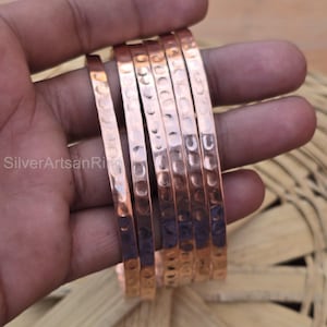 May include: A set of six copper bracelets with a hammered texture. The bracelets are stacked on top of each other and are a warm, reddish-brown color.