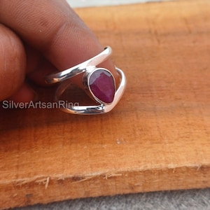 Könnte beinhalten: Ein silberner Ring mit einem tropfenförmigen Rubin-Edelstein. Der Ring hat ein Doppelband-Design.