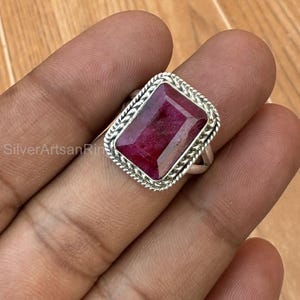 May include: A sterling silver ring featuring a large, rectangular, deep red gemstone. The gemstone is set in a decorative, textured bezel. The ring is displayed on a hand.