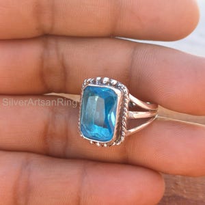 May include: A silver ring featuring a large, rectangular, light blue gemstone. The ring has a twisted band and a beaded edge around the gemstone.