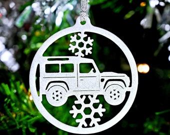 May include: A white, silver-colored Christmas ornament shaped like a circle with a cutout design of a Land Rover and snowflakes.