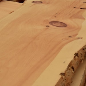 Könnte beinhalten: Nahaufnahme einer hellbraunen Holzplatte mit natürlicher Kante. Die Holzmaserung ist sichtbar, mit Ästen und Farbvariationen. Die Platte scheint unfertig zu sein und für Holzbearbeitungsprojekte bereit zu sein.